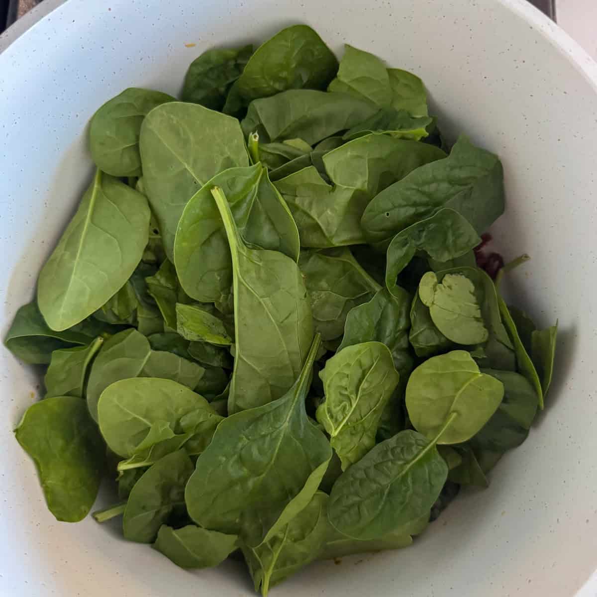 Spinach added to a pot on top of the cooking sun-dried tomatoes