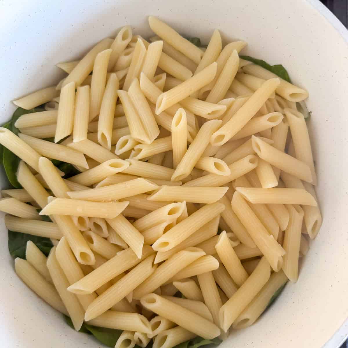 Pasta added on top of spinach and sun dried tomatoes in a pot