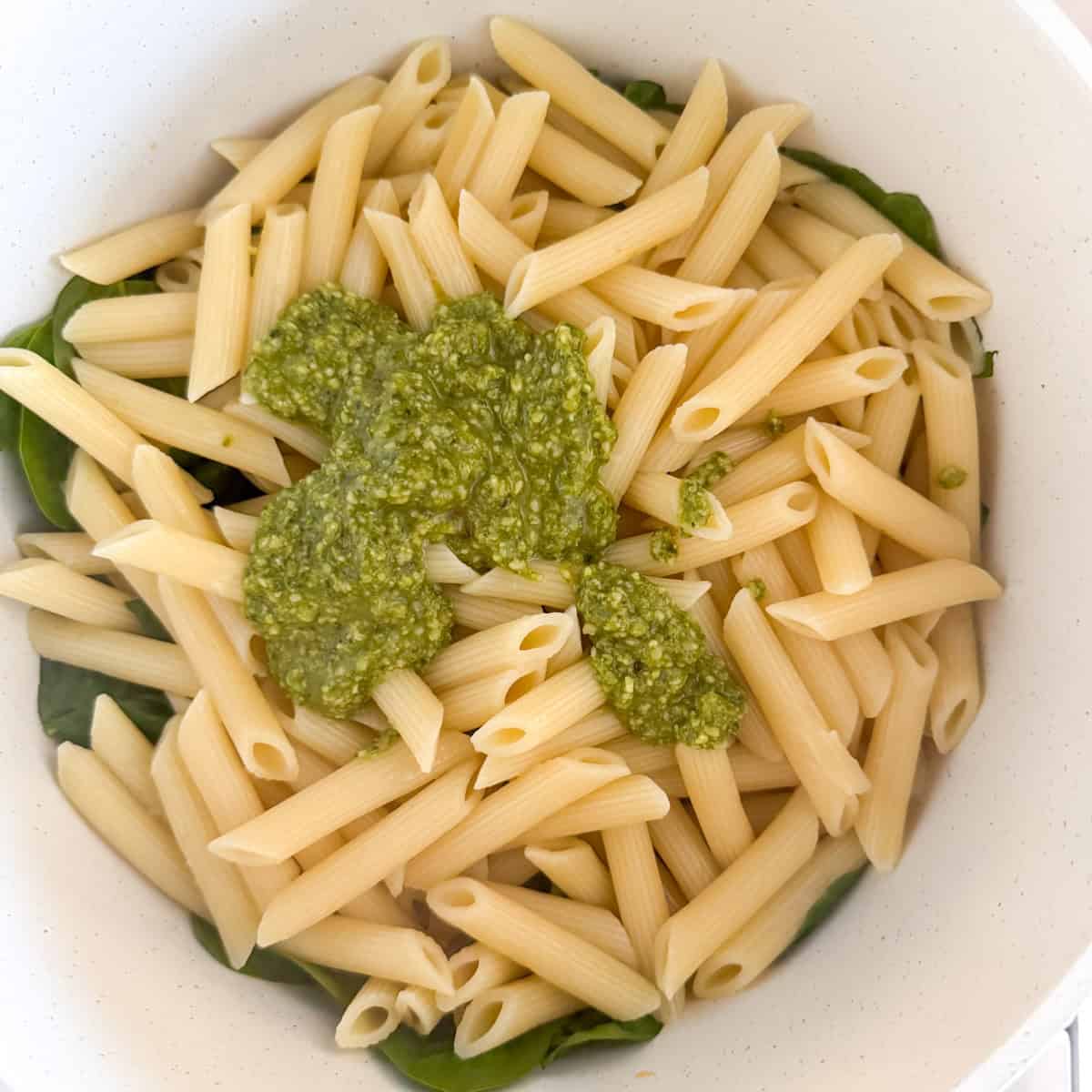 Pesto added on top of pasta, spinach, sun-dried tomatoes and garlic
