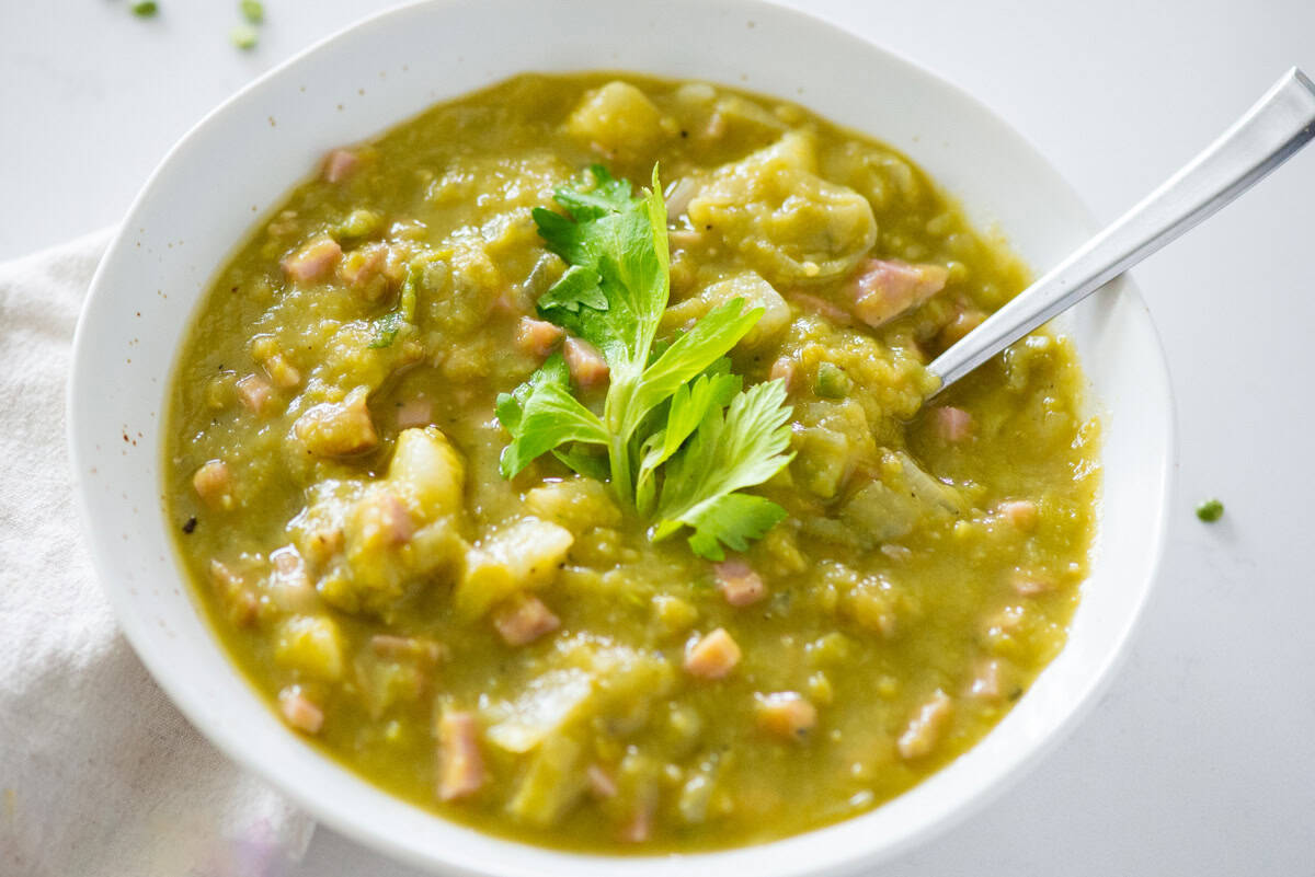 Close up view of split pea soup garnished with fresh celery leaves and a spoon sticking out one side and a napkin on the other side