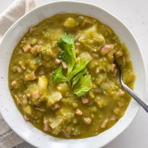 Overhead view of a bowl of split pea soup garnished with celery leaves and a spoon sticking out