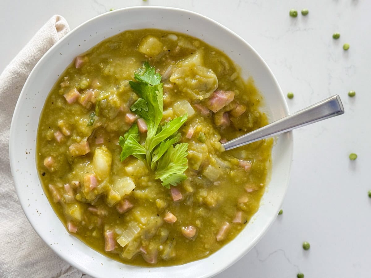 Overhead view of a bowl of split pea soup garnished with celery leaves and a spoon sticking out