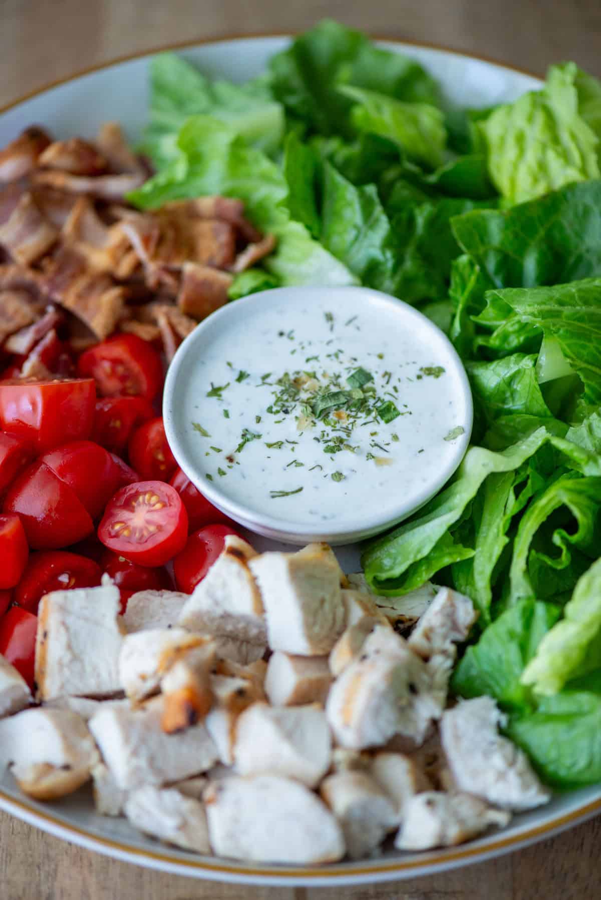 Overhead view of a middle of a plate filled with Chicken BLT Salad with ranch dressing in the middle