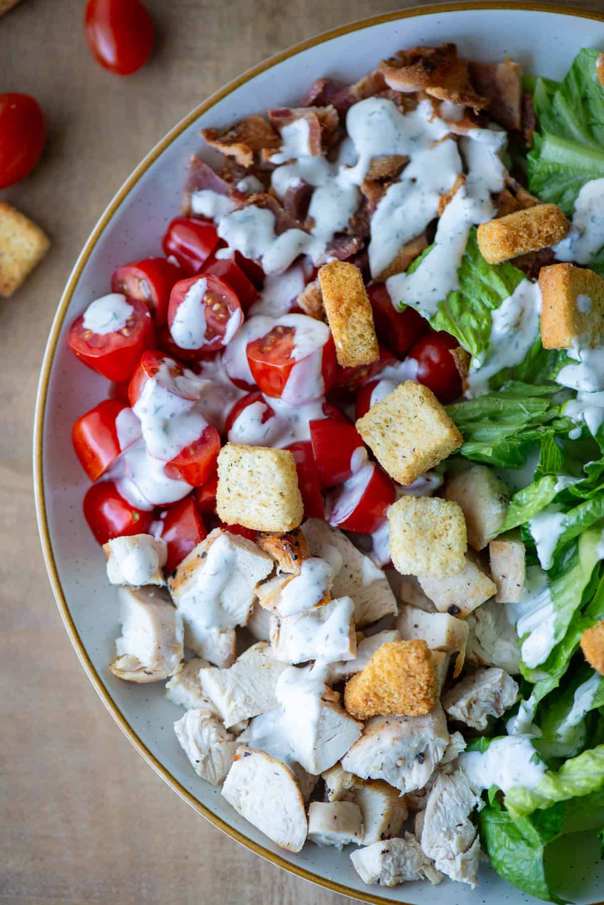 Overhead view of chicken BLT salad with ranch dressing drizzled across the salad and croutons on top