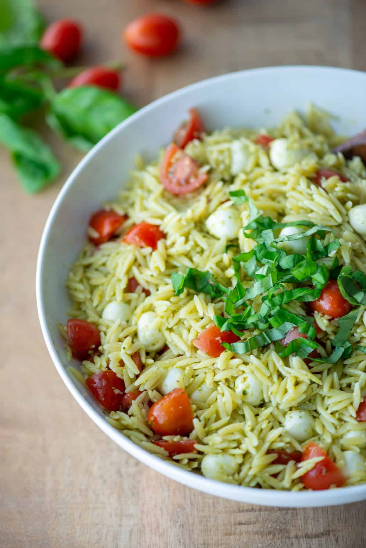Overhead view of pesto orzo pasta salad on a plate garnished with basil with some loose basil and cherry tomatoes in the background