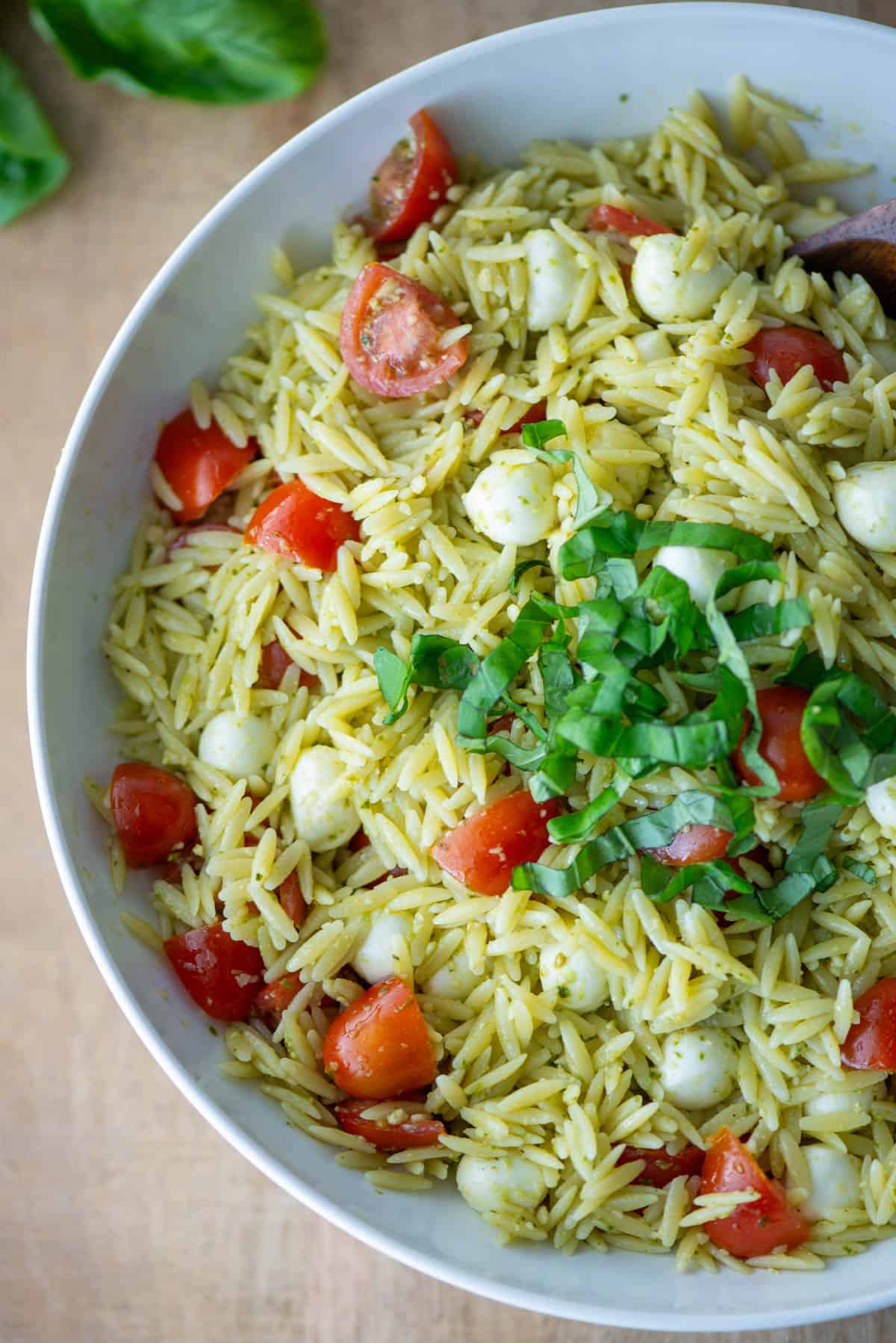 Overhead view of pesto orzo pasta salad on a plate garnished with basil with some loose basil in the background