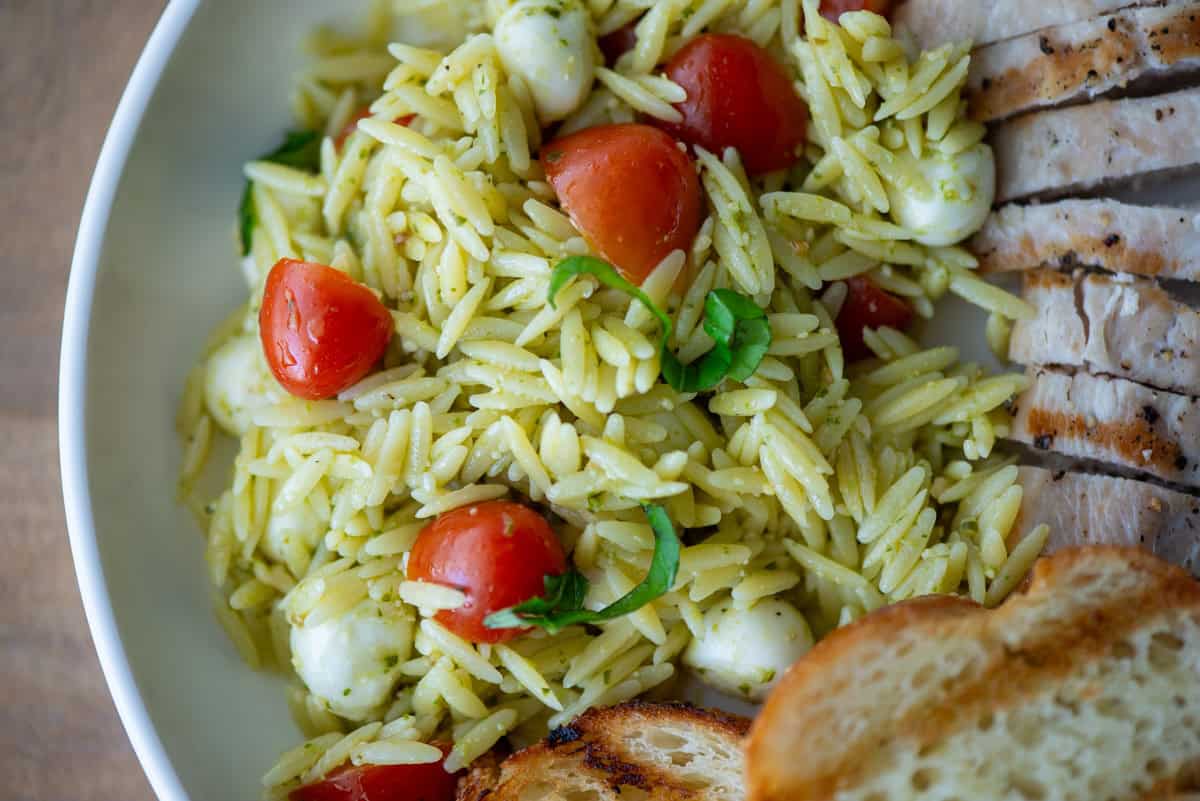 Overhead view of pesto orzo pasta salad on a plate next to grilled garlic bread and grilled chicken