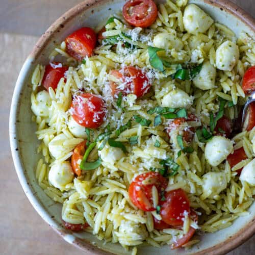 Overhead view of pesto orzo pasta salad on a plate garnished with sliced basil and parmesan cheese