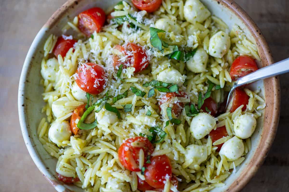 Overhead view of pesto orzo pasta salad on a plate garnished with basil and parmesan cheese with a fork sticking out