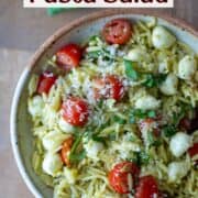 Overhead view of pesto orzo pasta salad on a plate garnished with sliced basil and parmesan cheese with a title overlay that says Pesto Orzo Pasta Salad