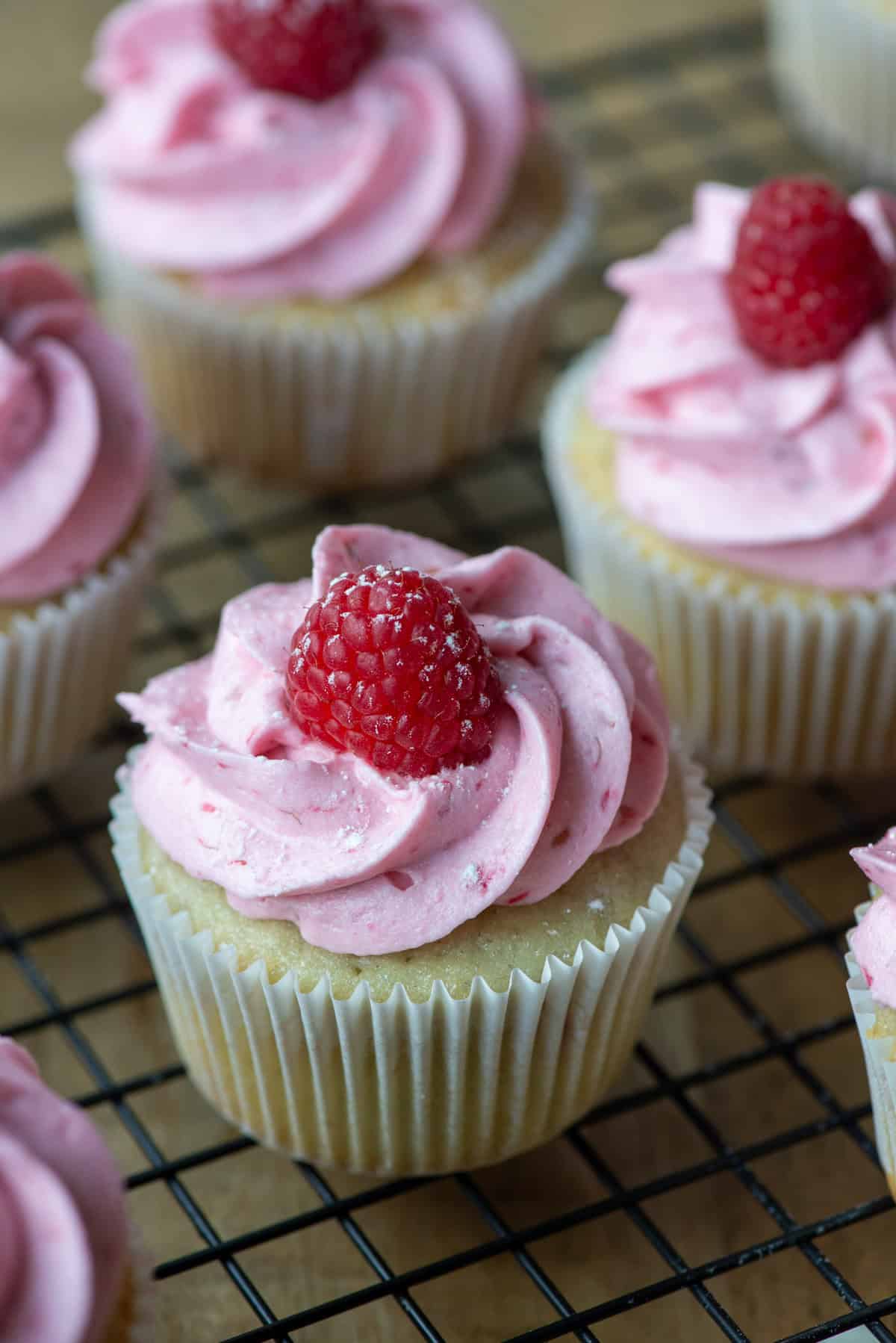 Overhead photo of raspberry white chocolate cupcakes where one is in focus in front with other partial cupcakes in view in the background
