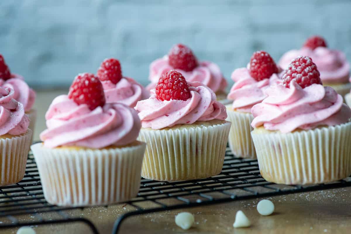 Side view of raspberry white chocolate cupcakes on a cooling rack with white chocolate chips scattered about