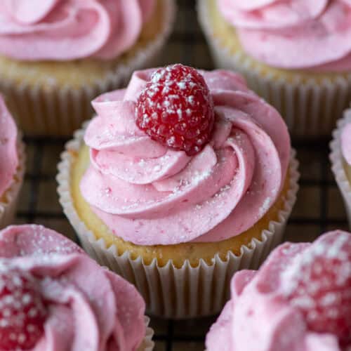 Overhead photo of raspberry white chocolate cupcakes where one is centered and surrounded by others in partial view