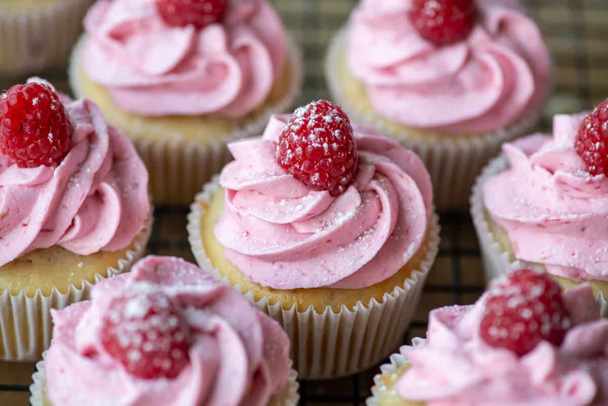 Overhead photo of raspberry white chocolate cupcakes where one is centered and surrounded by others in partial view