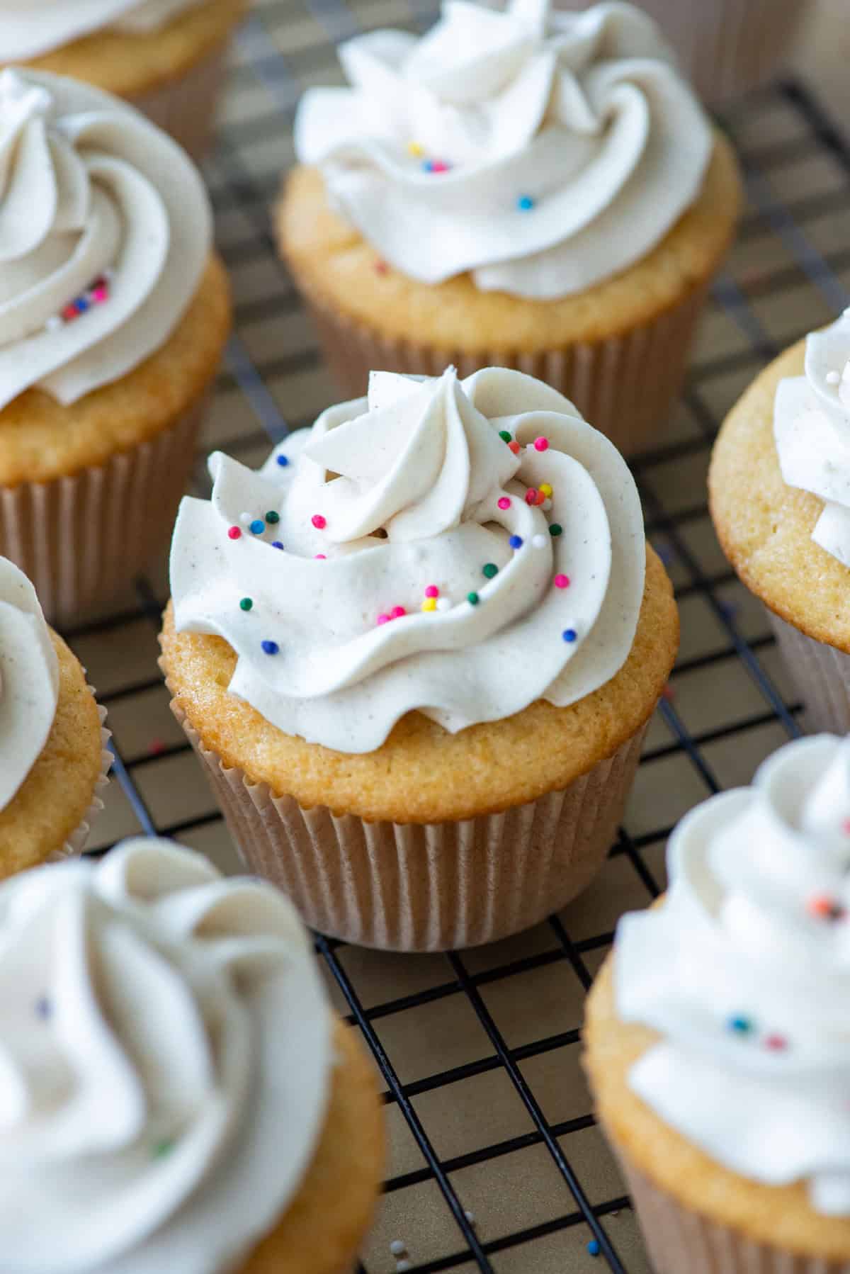 Close up overhead view focused on the center vanilla bean cupcake in a group of cupcakes on a black wire cooling rack