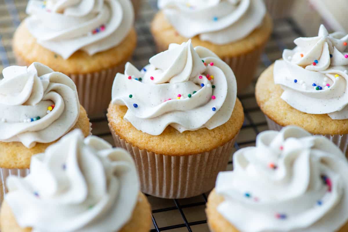 Close up overhead view focused of vanilla bean cupcakes on a black wire cooling rack