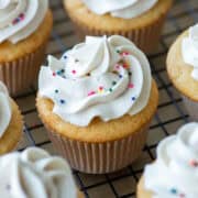 Close up view focused on one vanilla bean cupcake with vanilla bean buttercream with sprinkles surrounded by a partial view of other cupcakes with a title overlay that says Vanilla Bean Cupcakes at the top and another one that says With Vanilla Bean Buttercream at the bottom