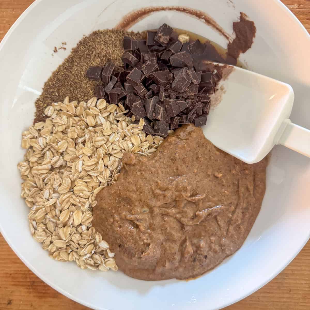Second step of making chocolate protein powder balls: add old fashioned oats, crunchy almond butter, chocolate chunks and flaxseed to the mixing bowl