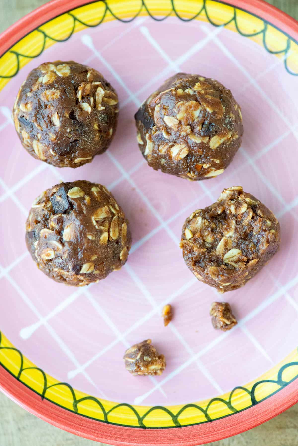 Overhead photo of 4 chocolate protein powder balls on a plate, one with a bite taken out and crumbs nearby