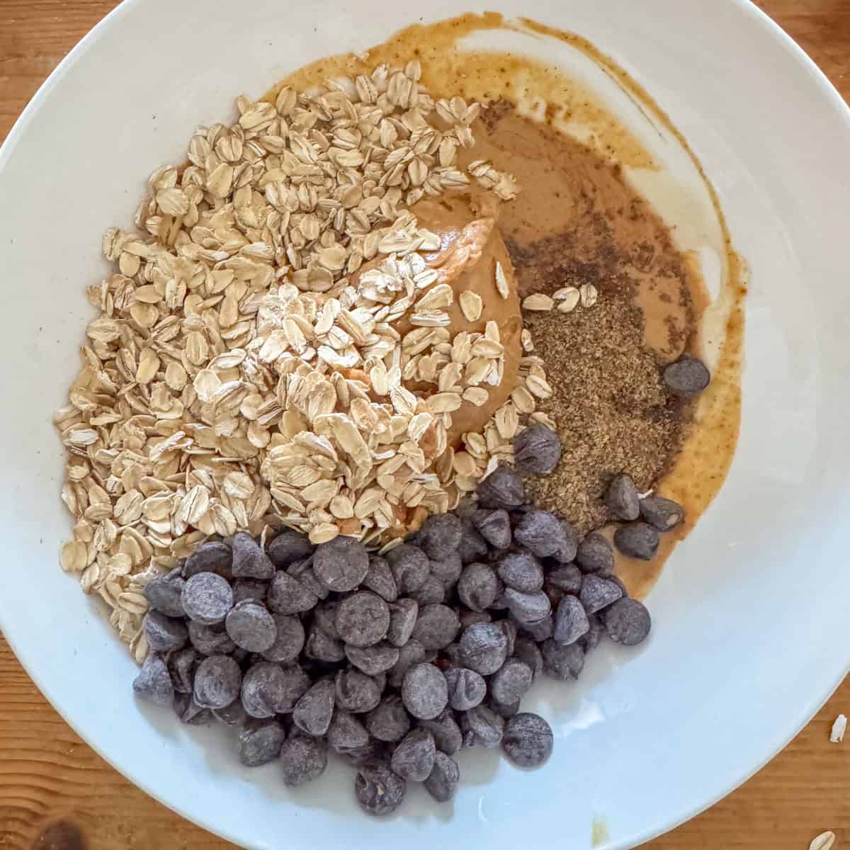 Step 2 of making no bake oatmeal peanut butter balls: add the crunchy peanut butter, old fashioned oats, ground flaxseed, maple syrup and chocolate chips to the bowl
