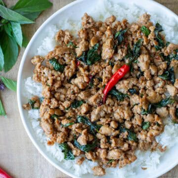 Overhead view of a partial plate of Thai Basil Chicken over a bed of white rice with Thai Basil in the background