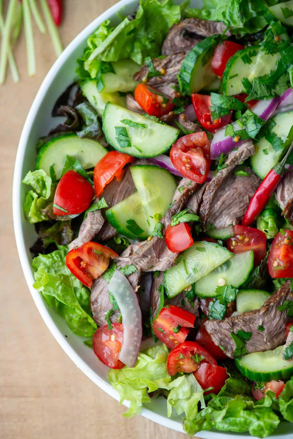 Overhead view of partial plate of Thai beef salad over a bed of red leaf lettuce with cilantro stems in the background