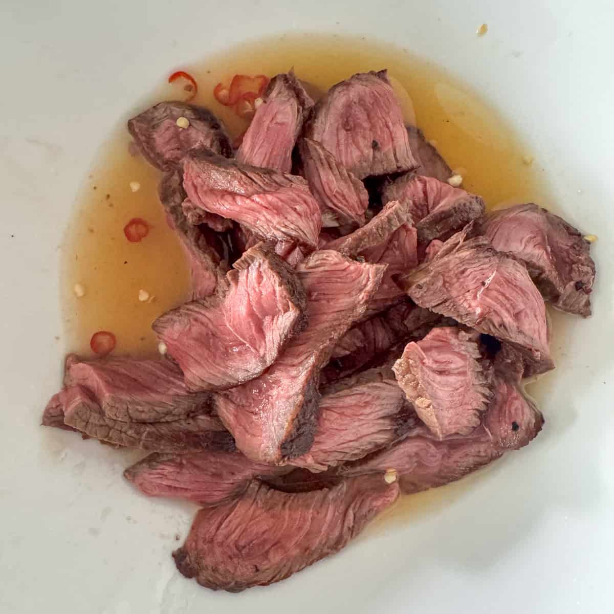 Close up of sliced top sirloin to top of the dressing for the Thai beef salad