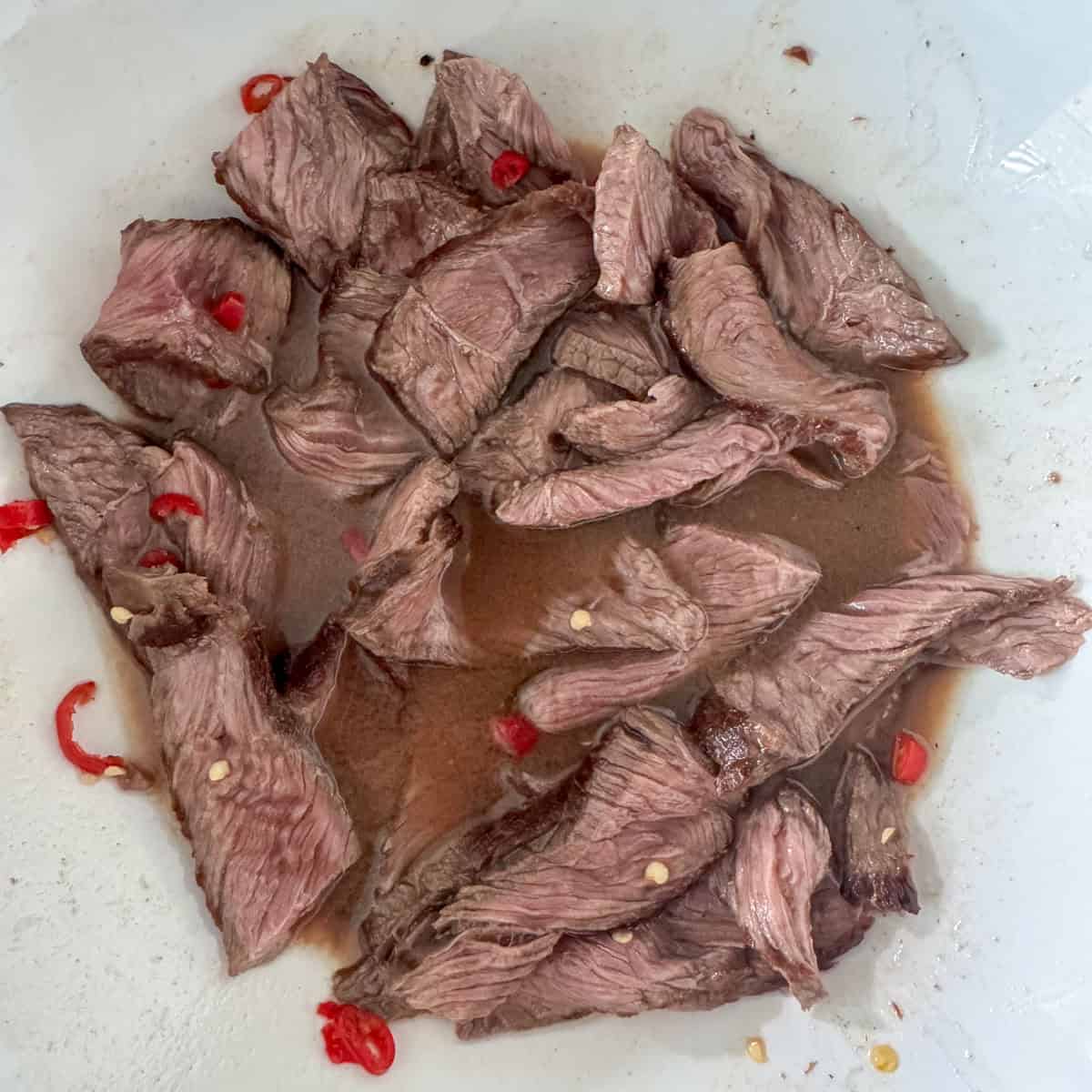 Close up of sliced top sirloin that's been tossed in the dressing for the Thai beef salad to show that the meat browns due to the lime juice