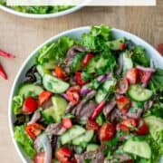 Overhead view of plate of Thai beef salad over a bed of red leaf lettuce with another partial plate in the background with a title overlay that says Thai Beef Salad