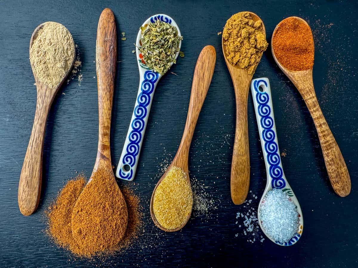 Spices needed to make homemade taco seasoning each on a different spoon: red chili powder, cumin, Mexican oregano, garlic powder, onion powder, paprika and salt