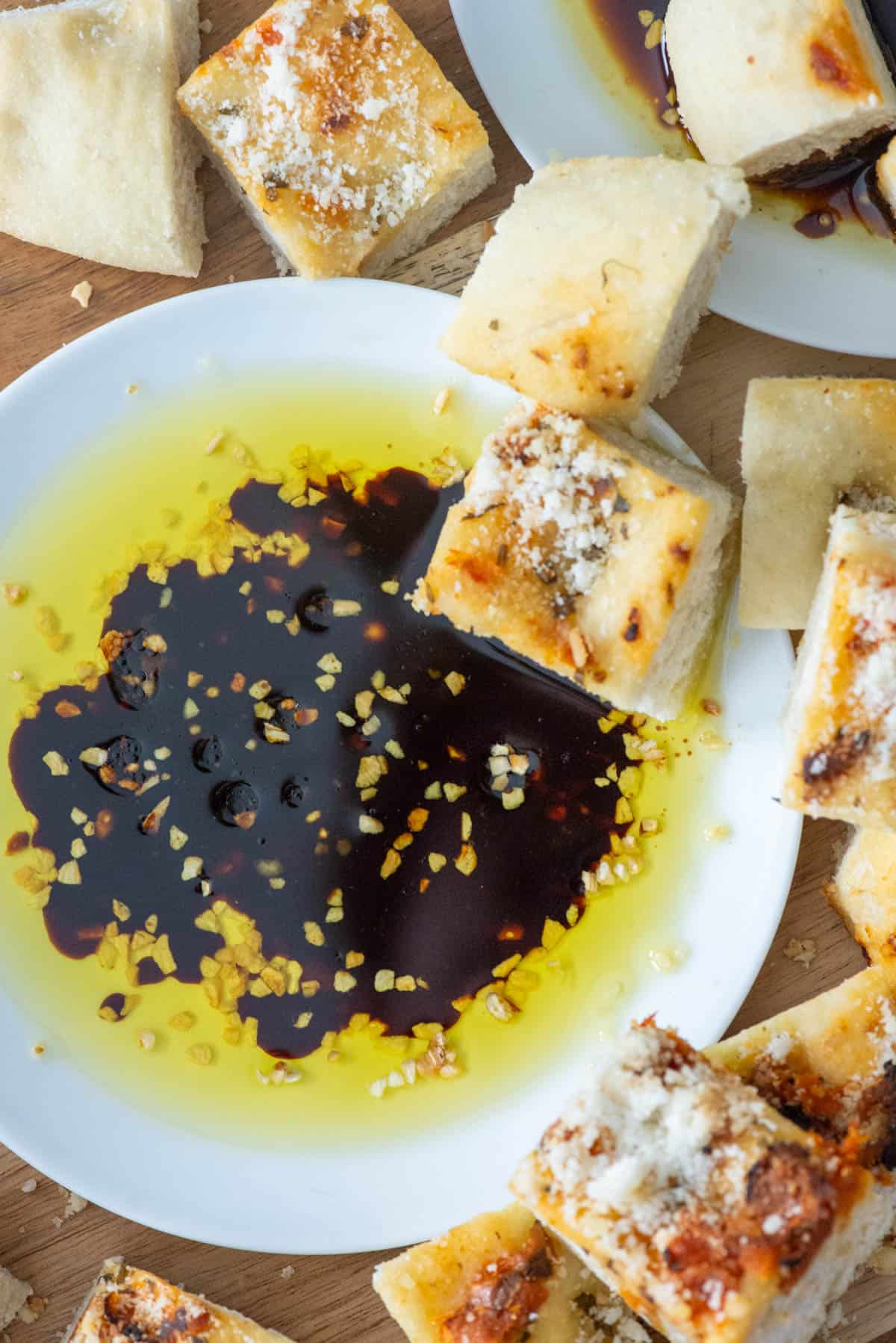 Overhead view of a small white plate filled with bread dipping oil made with dried minced garlic, olive oil and balsamic vinegar surrounded by cubes of bread