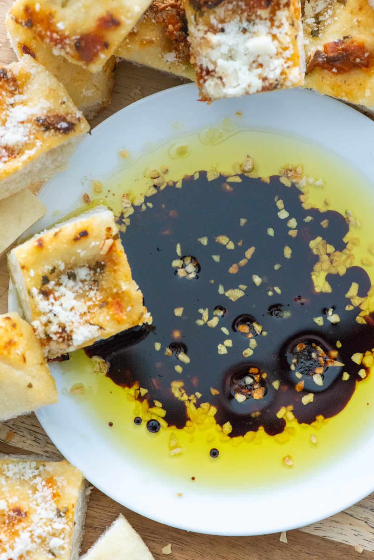 Overhead view of a small white plate filled with bread dipping oil made with dried minced garlic, olive oil and balsamic vinegar surrounded by cubes of bread