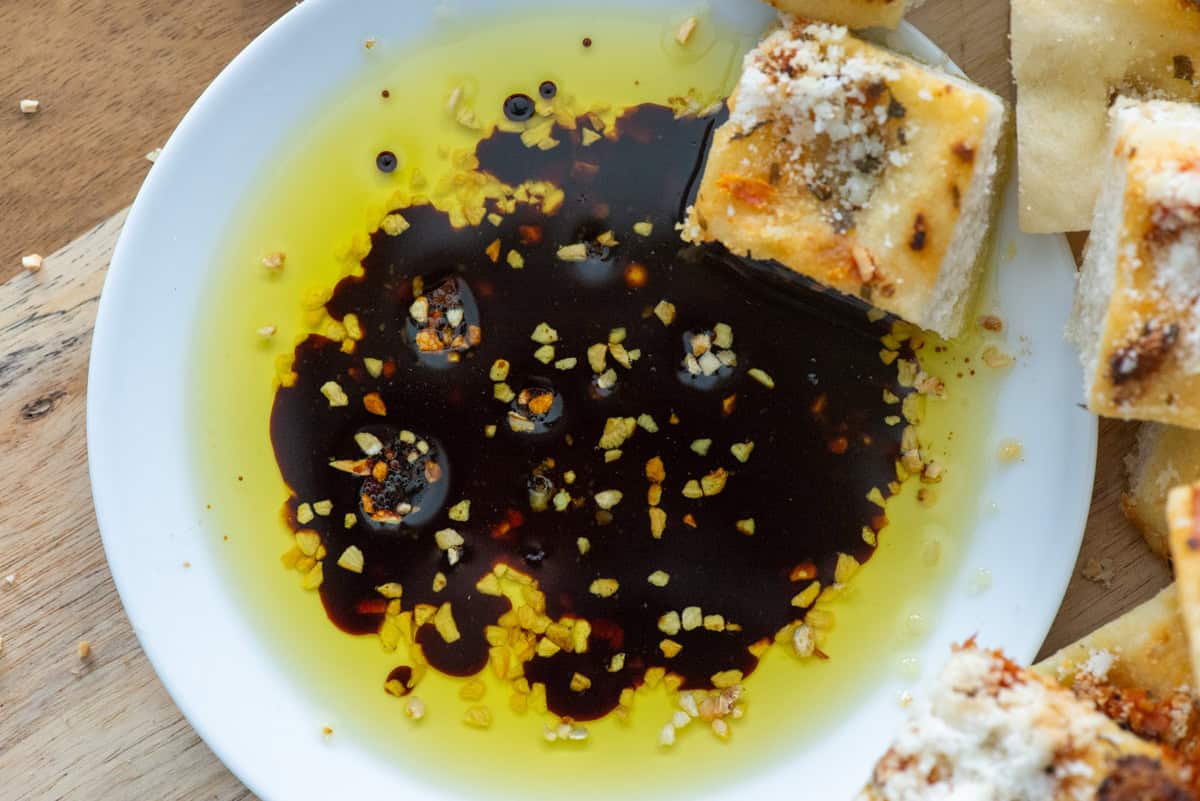 Close up overhead view of bread dipping oil on a small white plate with a cube of bread in the oil and more cubes of bread to the side of the plate