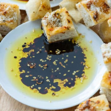 Overhead view of a small white plate filled with bread dipping oil which is dried minced garlic, olive oil and balsamic vinegar surrounded by cubes of bread