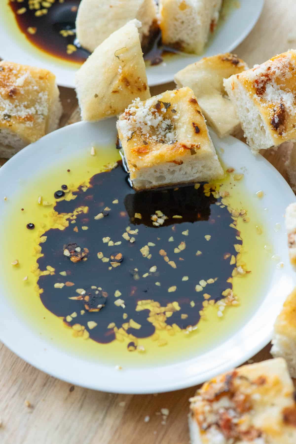 Overhead angled view of a small white plate filled with bread dipping oil made with dried minced garlic, olive oil and balsamic vinegar surrounded by cubes of bread