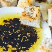 Overhead angled view of a small white plate filled with bread dipping oil which is dried minced garlic, olive oil and balsamic vinegar surrounded by cubes of bread with a title overlay that says Bread Dipping Oil