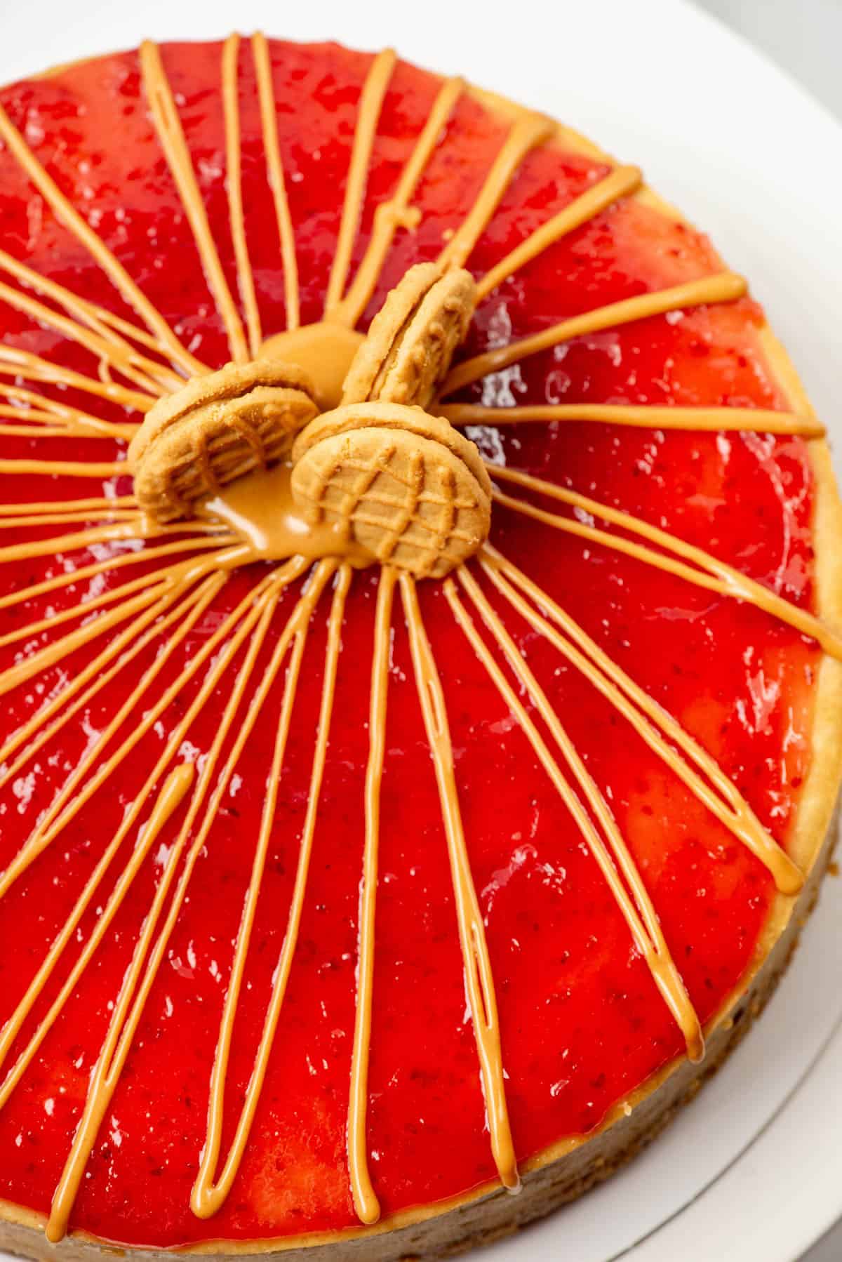 Overhead view of a partial peanut butter and jelly cheesecake decorated with peanut butter drizzle and three cut Nutter Butter cookies