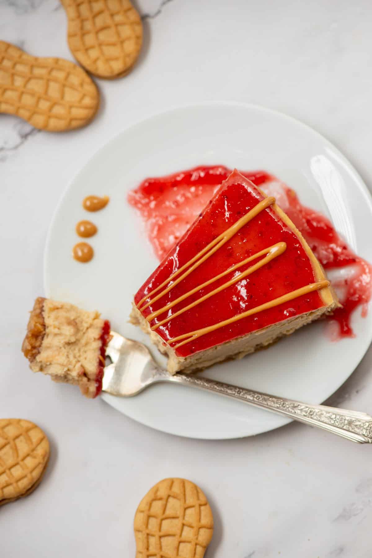 Overhead view of a slice of peanut butter and jelly cheesecake with peanut butter drizzle on a plate with a fork and a bite taken out