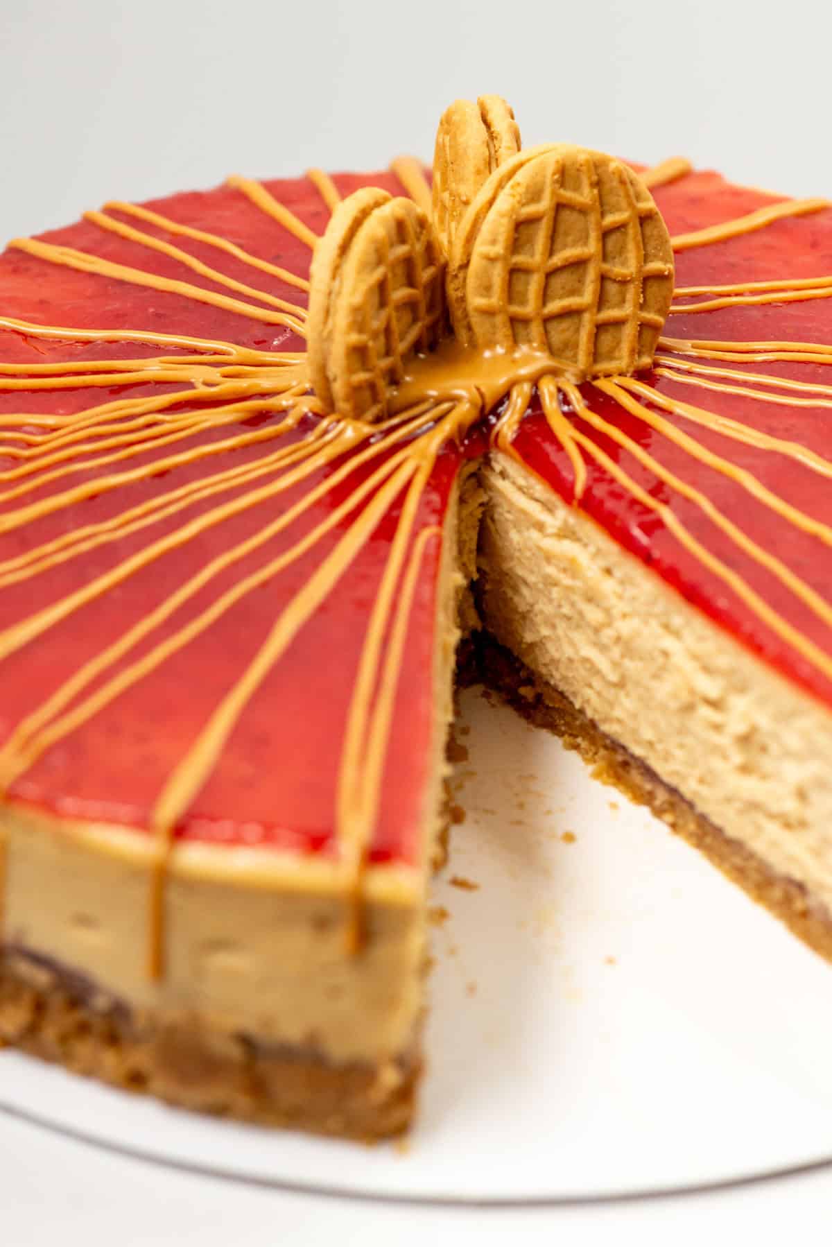 Overhead view of a partial peanut butter and jelly cheesecake decorated with peanut butter drizzle and three cut Nutter Butter cookies with a slice removed so that you can see the inside of the cheesecake