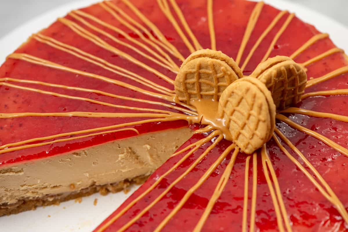 Overhead partial view of a peanut butter and jelly cheesecake with a peanut butter drizzle that has a slice taken out and where the focus is on the Nutter Butter cookies on top