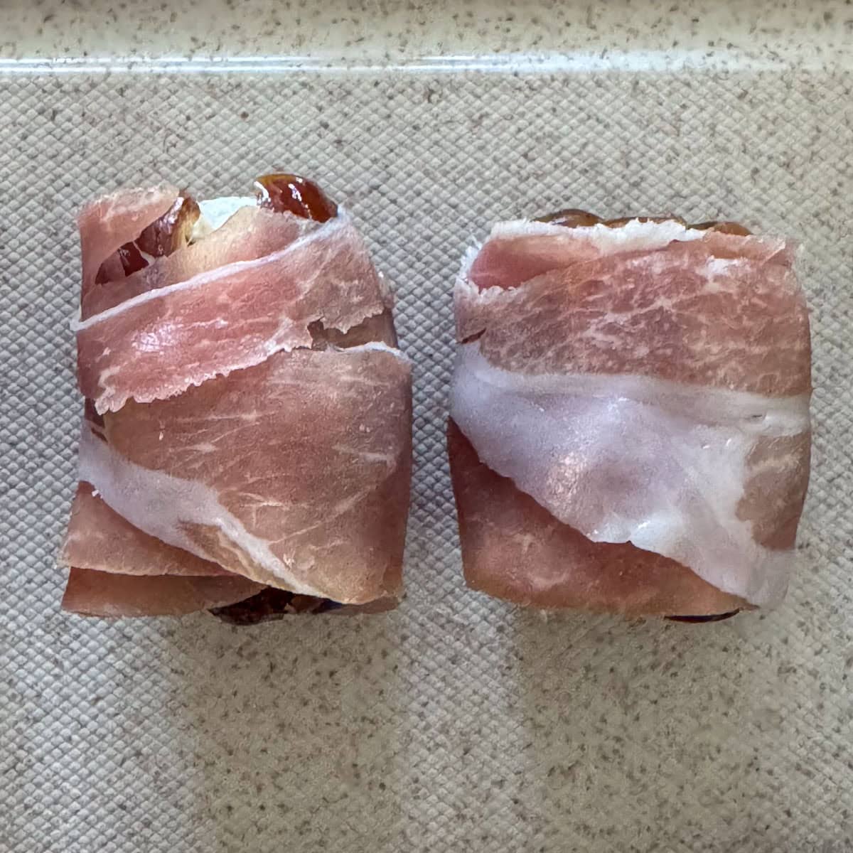 Overhead view of two dates wrapped with prosciutto,