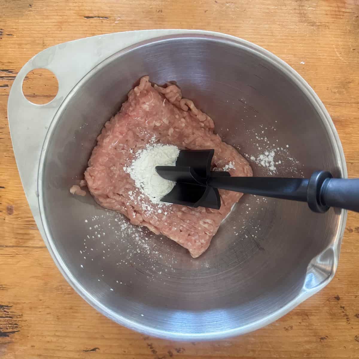 Overhead view of a medium bowl with ground chicken in a bowl with cornstarch on top with a meat chopper on the side