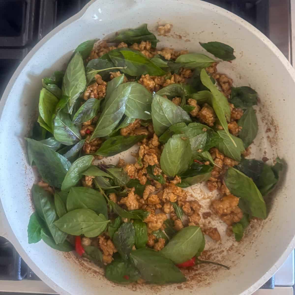 Overhead view of Thai basil that's been added to the skillet with the cooking chicken