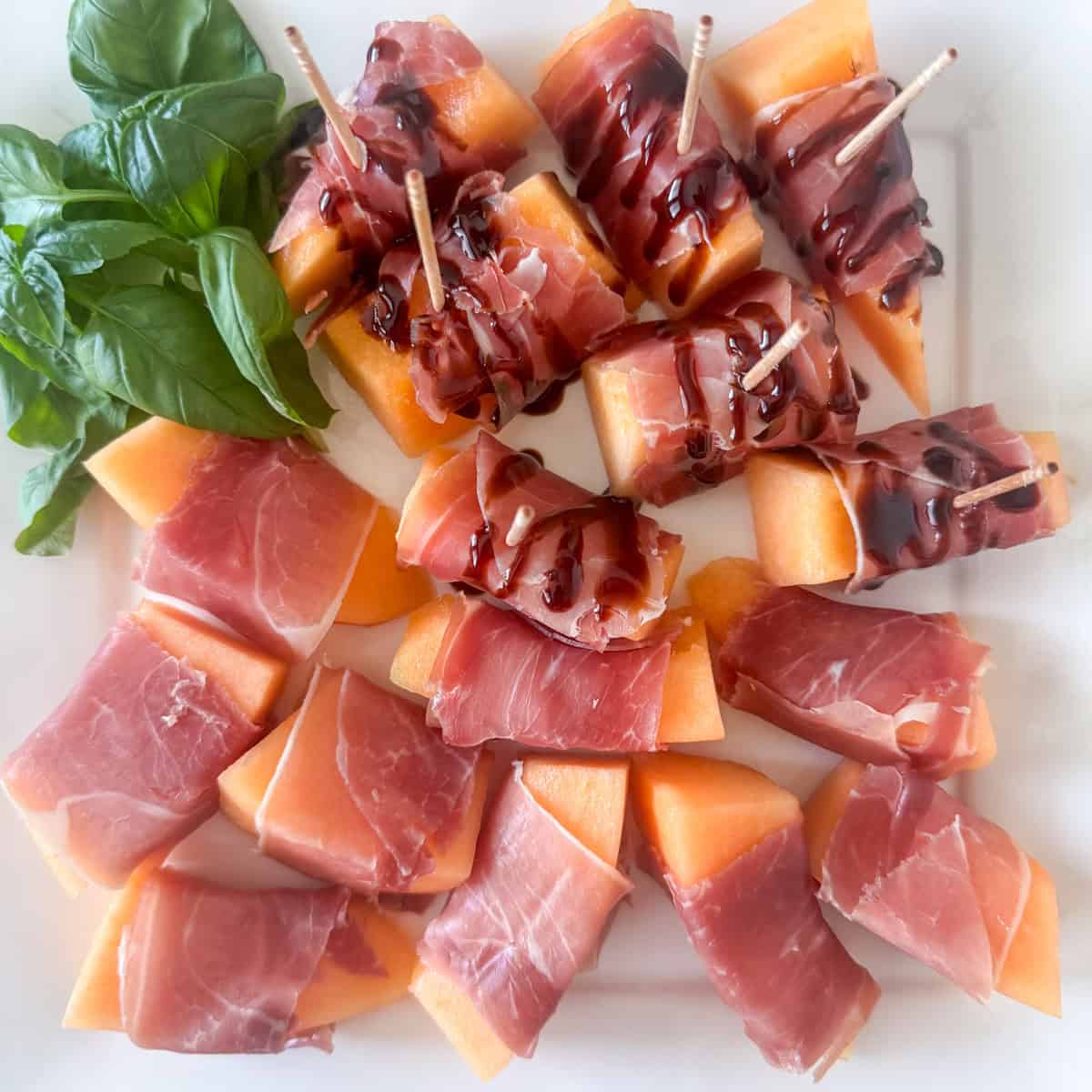 Step 3 in making prosciutto wrapped melon: wrap the prosciutto around the melon and press firmly to secure the prosciutto. Drizzle some or all with optional balsamic glaze. Add an optional toothpick to the ones with balsamic glaze for easier handling.