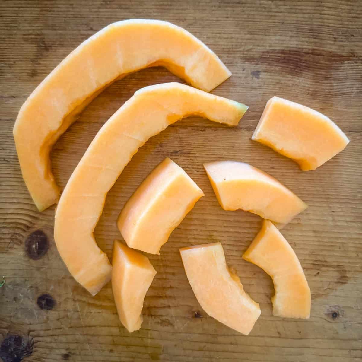 Step 2 in making prosciutto wrapped melon: cut the cantaloupe into slices and then smaller pieces about 2 inches in length