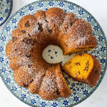 Overhead view of a whole pumpkin date bread made in a bundt pan with powdered sugar sprinkled on top. One slice has been cut and laid on its side so that the inside of the bread is visible.