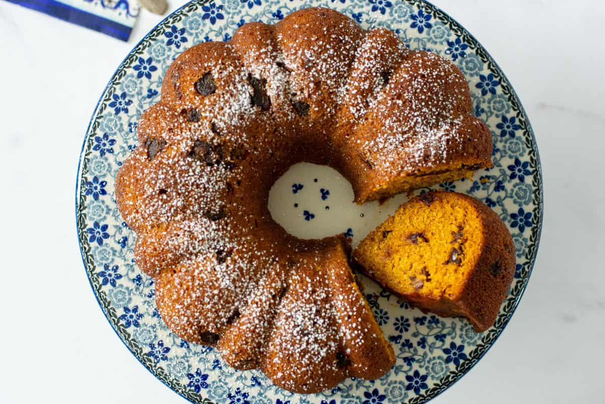Overhead view of a whole pumpkin date bread made in a bundt pan with powdered sugar sprinkled on top. One slice has been cut and laid on its side so that the inside of the bread is visible.