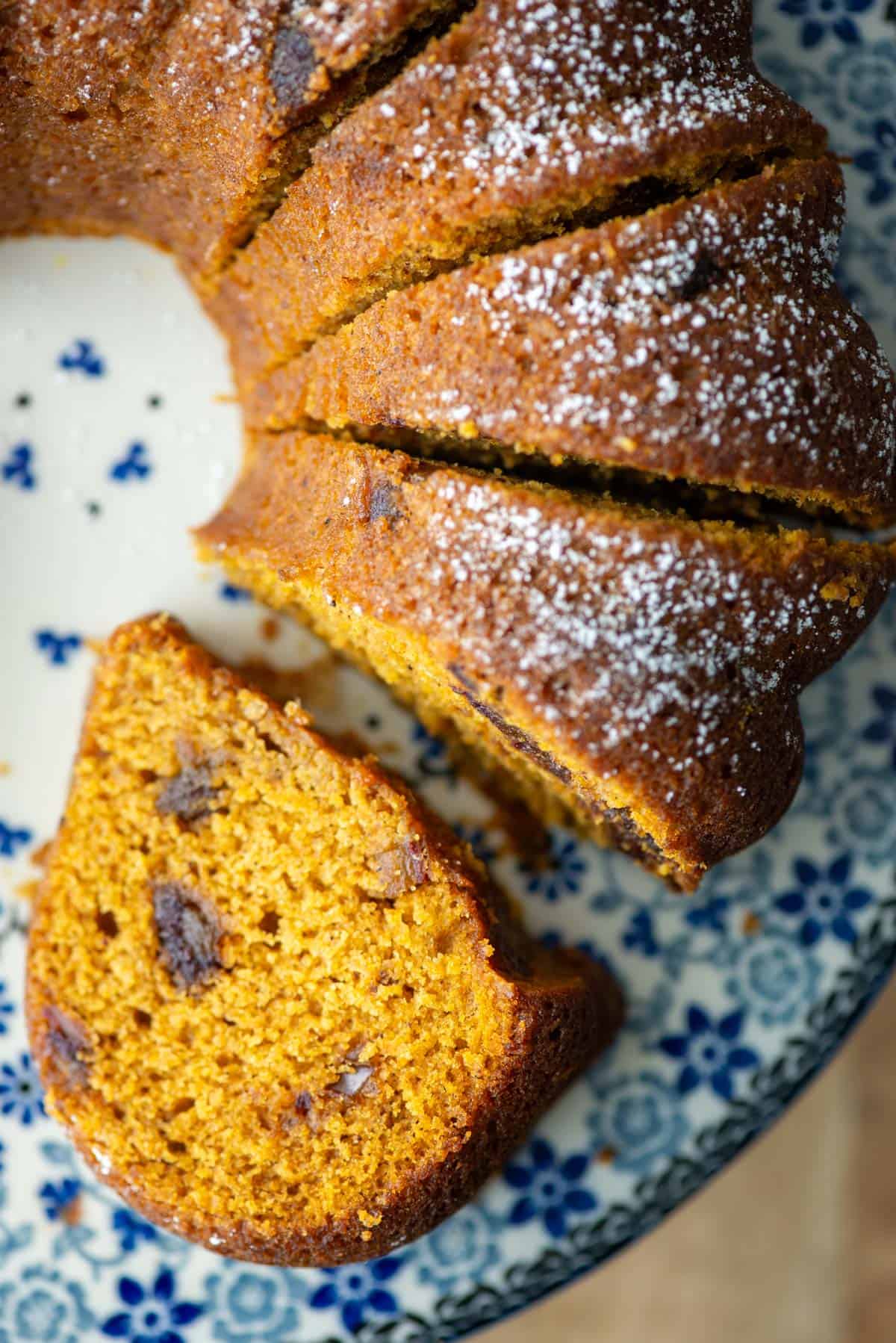 Overhead photo of a partial bundt of pumpkin date bread on a cake platter. One slice is lying on its side so that you can see the inside of the bread and four other upright slices are also visible in the photo.