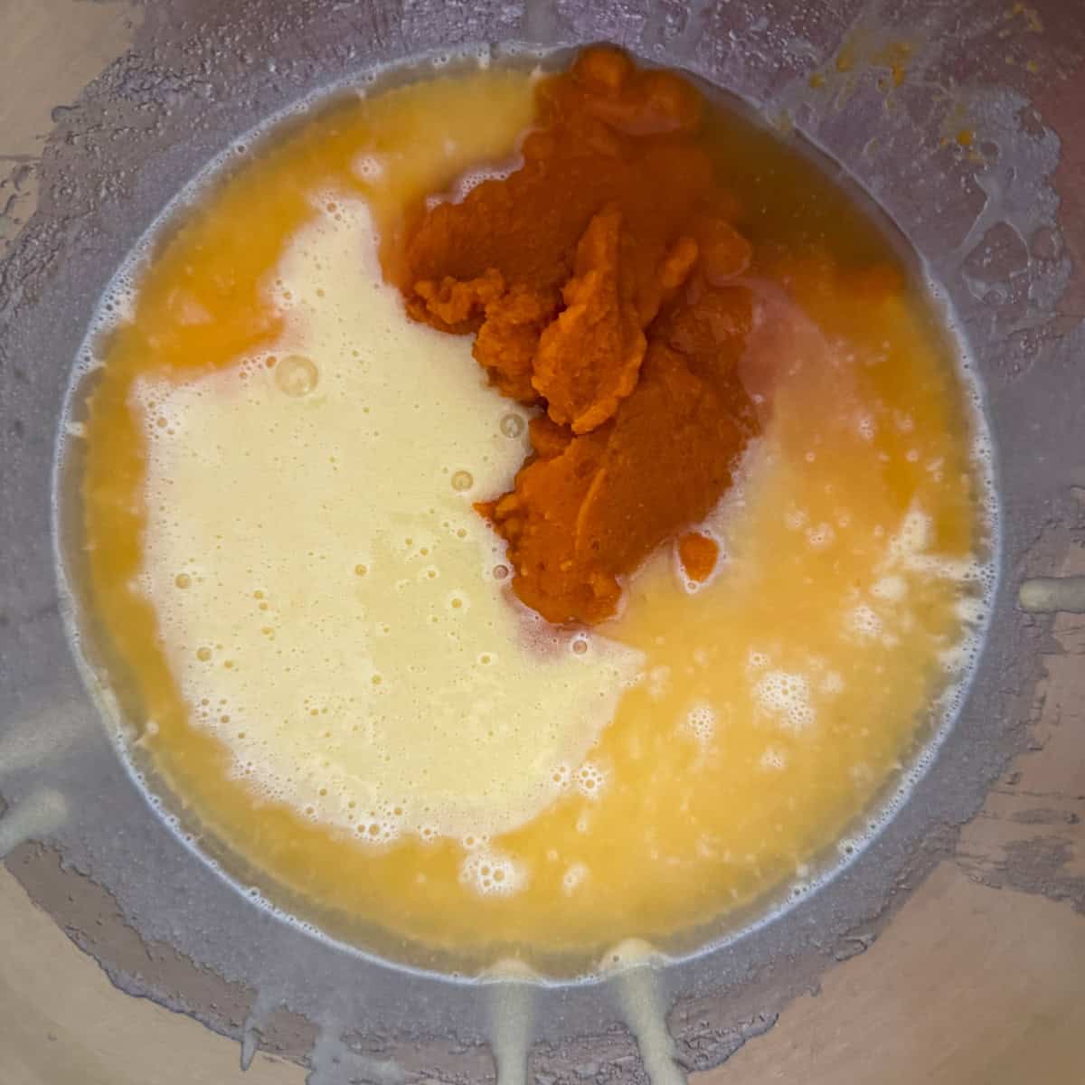 Mixing bowl filled with pumpkin puree and water on top of sugar, oil and eggs