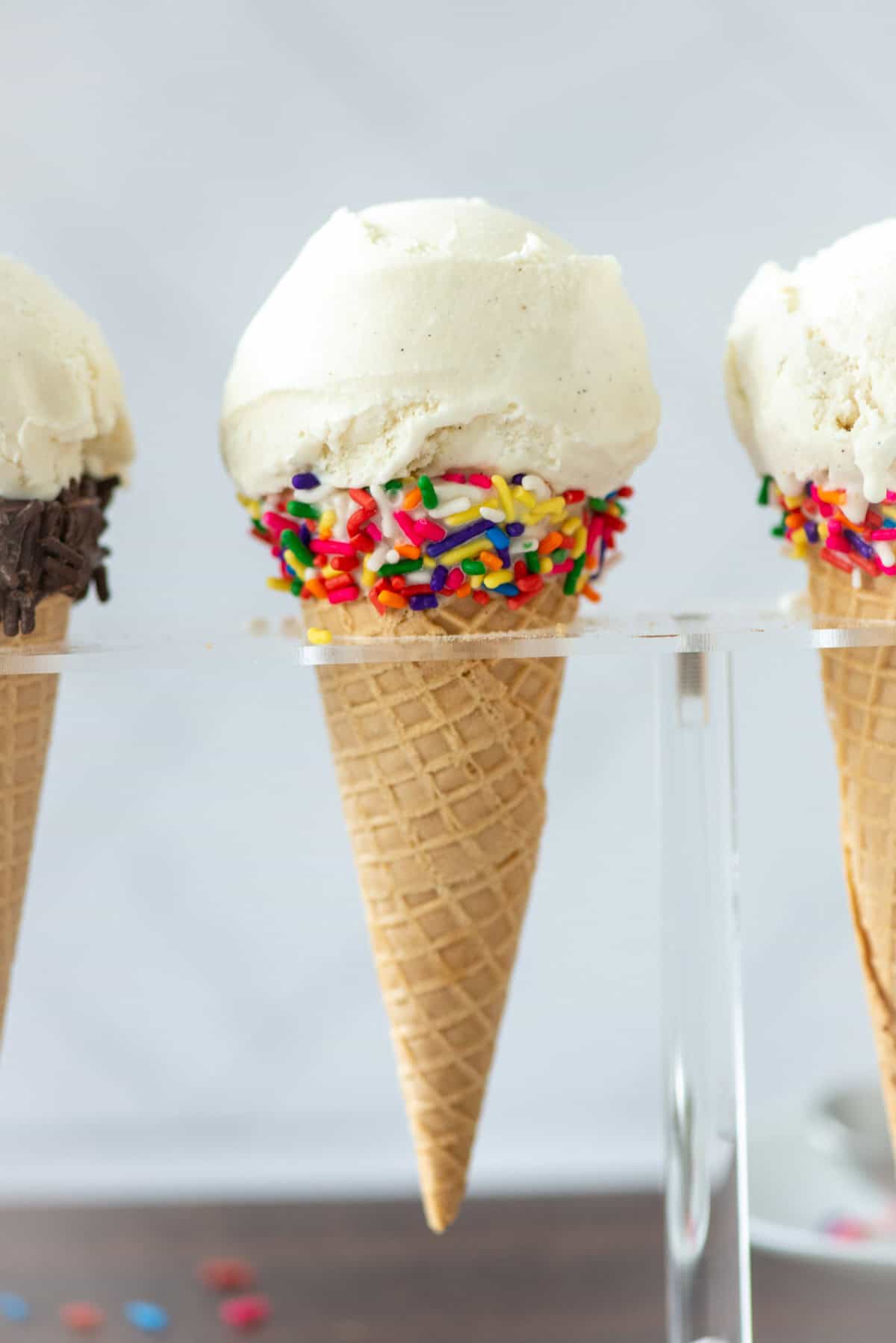 Side view of one whole and 2 partial homemade vanilla bean ice cream cones in sugar cones in an ice cream holder